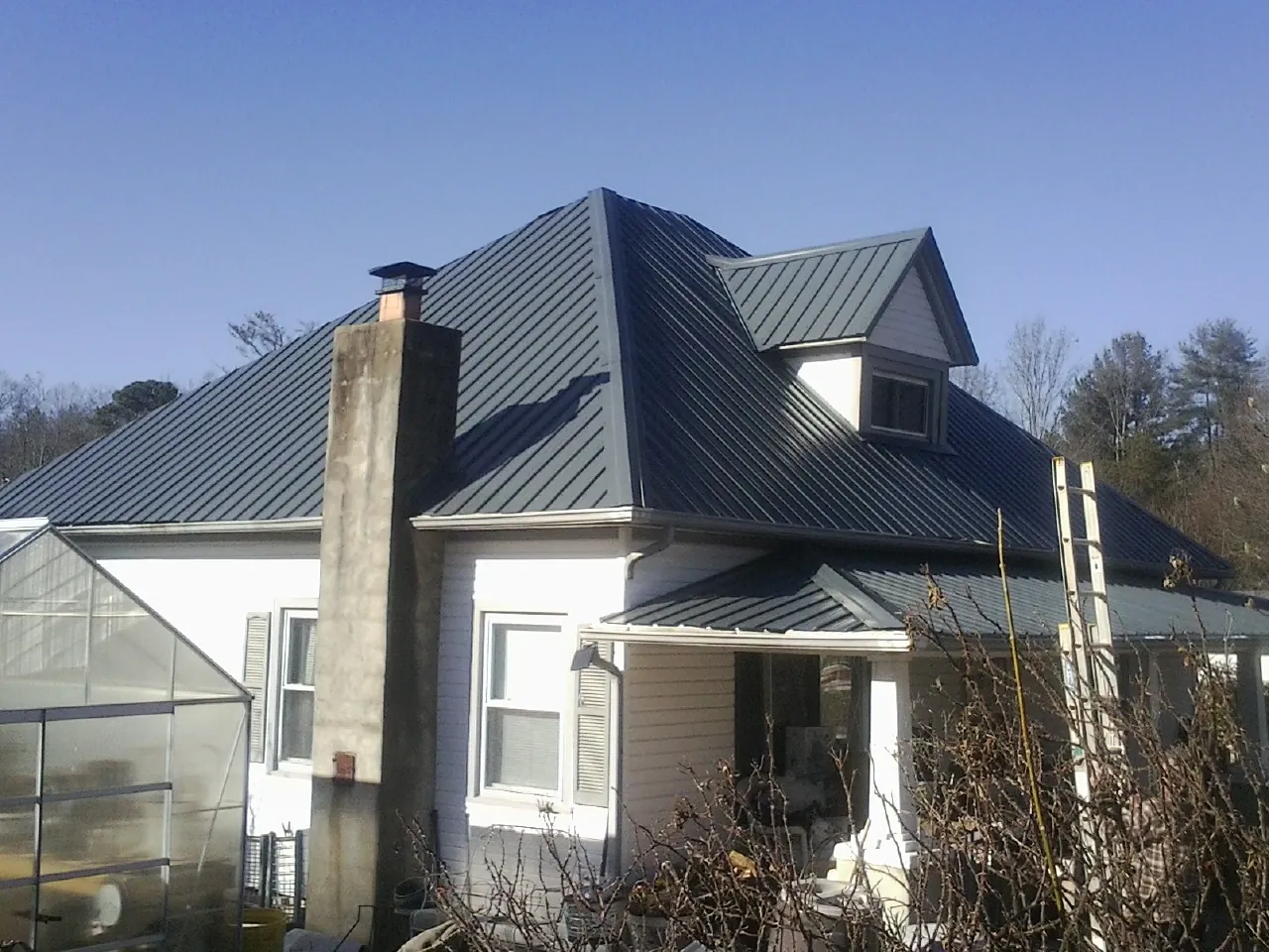Dark blue standing seam metal roof on a white farmhouse with dormer — Slate & Tile Roof Repair by Roofing Brothers in Seligman