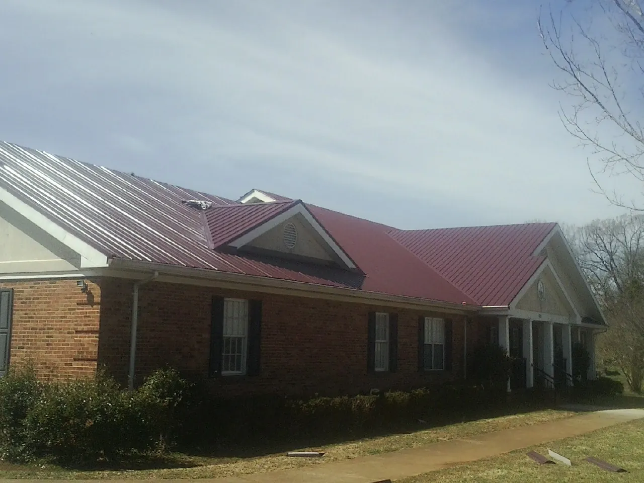 Red metal roof with gabled entries on a long brick building, from a Hail Damage Roof Repair job in Seligman