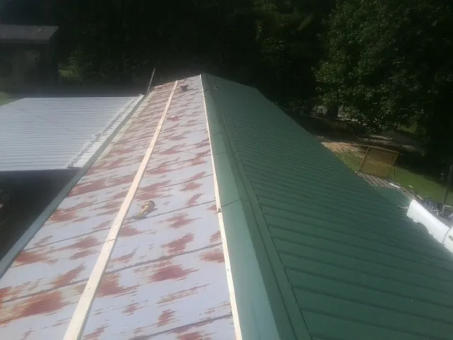 Old rusted panels beside newly installed green metal roofing — Wind Damage Roof Repair by Roofing Brothers in Seligman