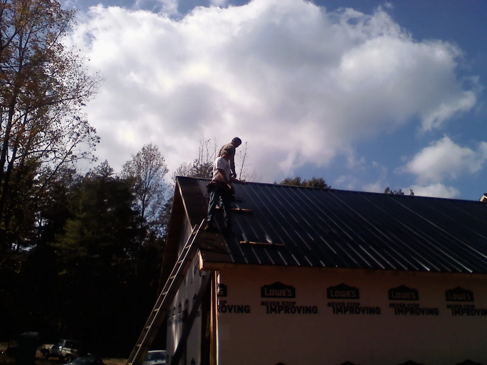 Roofer fastening dark metal panels high against a cloudy sky, from a Roof Inspection job in Seligman